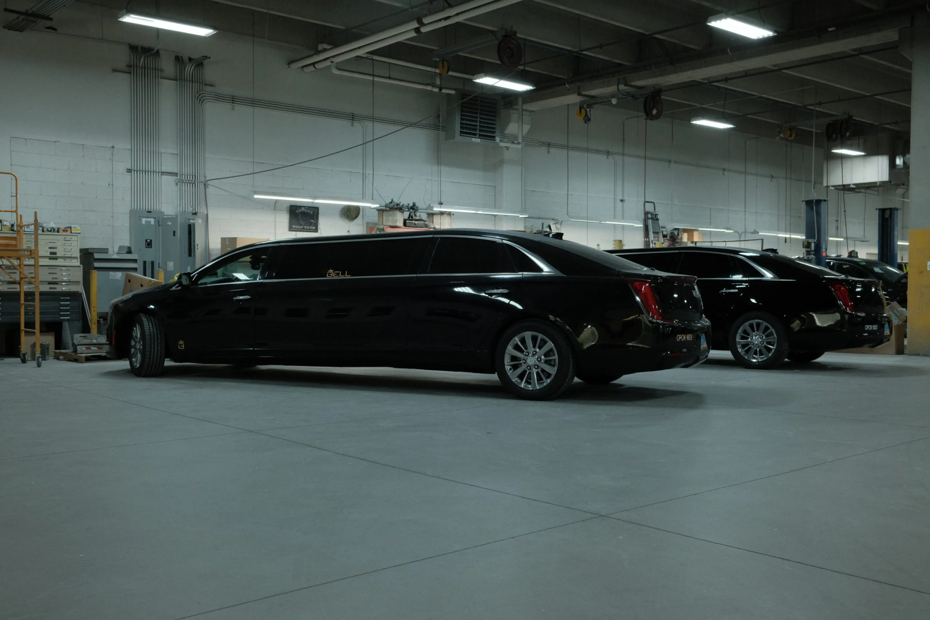 A black limo parked in a warehouse with other cars.