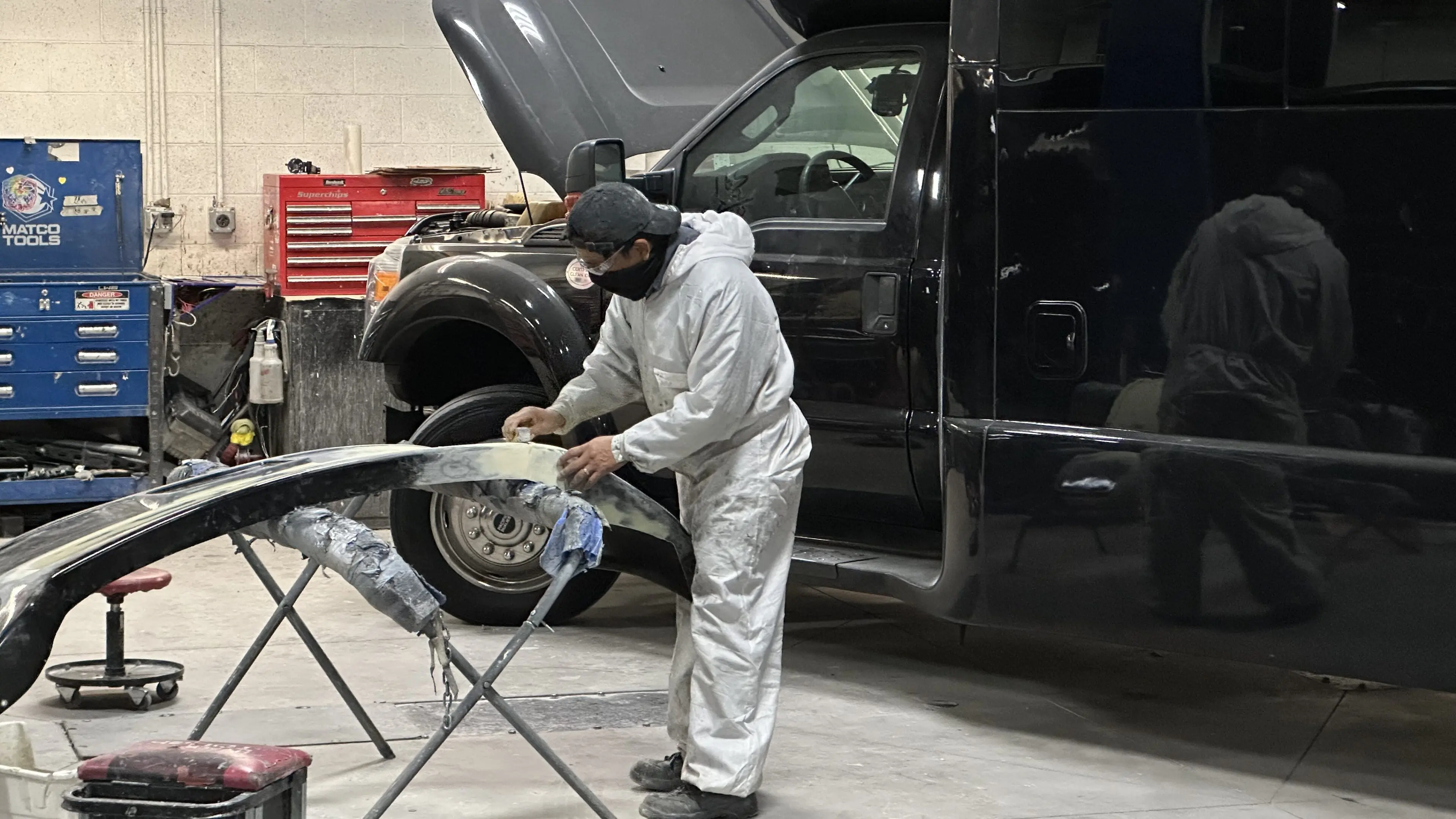 A man in white coveralls and black helmet working on an suv.