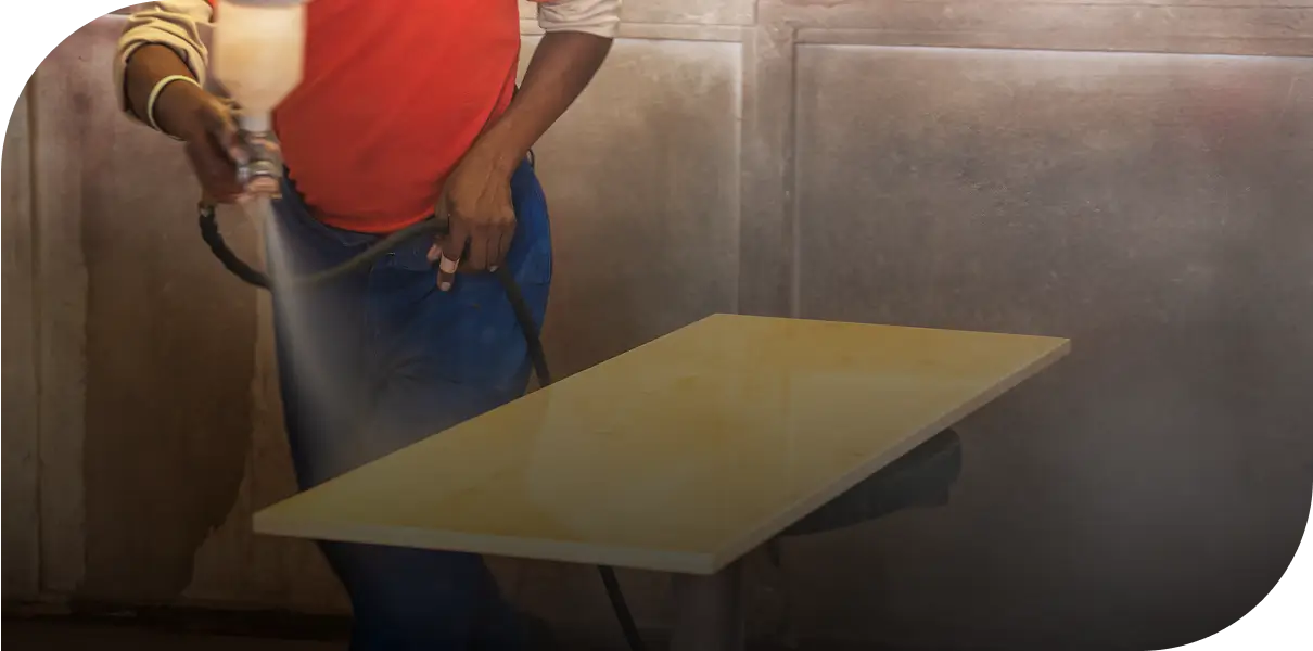 Person spray painting a wooden board in a workshop.
